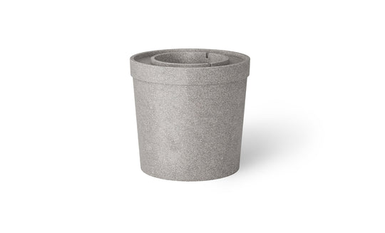 The Signature Ice Basin by Ledge Lounger is a cylindrical gray trash can featuring a stone-like texture and top slot, designed for waste collection. Its minimalist design resembles an umbrella base, making it ideal for both indoor and outdoor use.