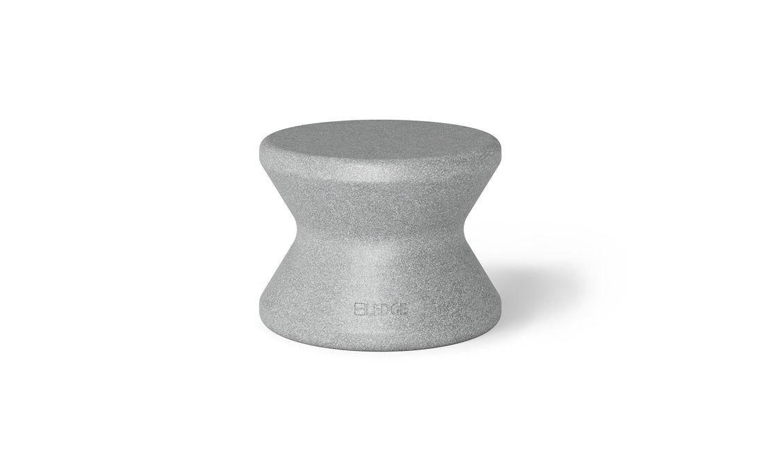 The Signature Standard Side Table by Ledge Lounger is a gray hourglass-shaped stool with a textured surface and smooth, curved design, perfect for in-pool use. The name BLØK is subtly engraved near the base, set against a plain white background.