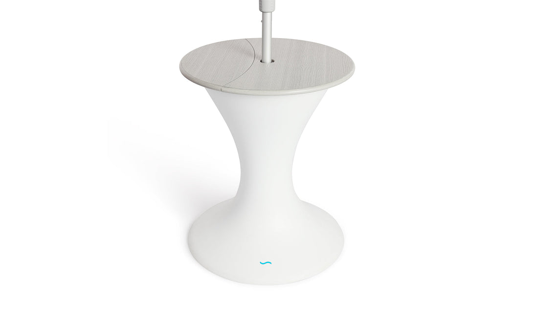 The Autograph Umbrella Stand Ice Bin by Ledge Lounger features a sleek design with a modern white pedestal base, a round gray top, and a central pole resembling an outdoor table. The flared base mimics an umbrella stand and showcases the small blue logo near the bottom.