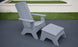 A Ledge Lounger Mainstay Adirondack Ottoman and matching chair sit on the dark patio. In the background, lush green grass borders a short white wall, creating a serene setting with high-quality materials.