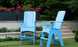 Two oversized Mainstay Adirondack Tall chairs by Ledge Lounger in light blue mark the ideal outdoor lounge setting. Set on the grass, concrete steps ascend behind with pink flowers flourishing. The vibrant garden scene is enhanced by built-in bottle openers for added convenience.