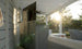 A sunlit outdoor patio features a large TV atop the Mainstay Bar Credenza - Final Sale by Ledge Lounger. White seating is partially sunlit, with trees in the background. Sun rays create lens flares, making the scene feel bright and inviting.