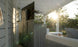 A sunlit outdoor patio features a large TV atop the Mainstay Bar Credenza - Final Sale by Ledge Lounger. White seating is partially sunlit, with trees in the background. Sun rays create lens flares, making the scene feel bright and inviting.