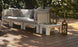 A serene outdoor deck highlights the Ledge Lounger Mainstay Sectional Relaxed Endcap with gray cushions and many pillows for ultimate comfort. Its set on wooden floorboards with two large lanterns nearby, while trees provide a shaded, peaceful backdrop.