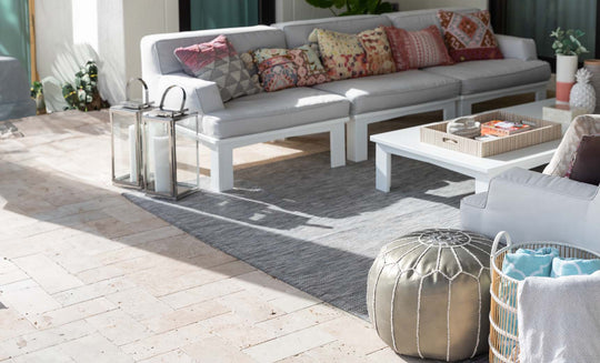 The outdoor patio showcases a Ledge Lounger Mainstay Sectional Right Armchair with colorful pillows, a white coffee table decorated with items, a gray rug, and a metallic pouf. Two lanterns and a basket of blankets complete the cozy setup on the tiled floor.
