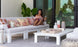 A woman lounges in a Mainstay Sectional Right Armchair by Ledge Lounger, accessorized with a vibrant cushion set, sipping her drink while reading a magazine. A white coffee table holds decorative items nearby, surrounded by lush green plants and sleek glass doors in the background.