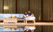 Beside the pool, a couple relaxes on the Mainstay Sectional Relaxed Right Corner by Ledge Lounger. Comforted by plush cushions, they smile as large glass windows and patterned curtains behind them reflect the tranquil scene.