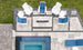 An aerial view of a modern patio shows six white chairs with blue cushions encircling a rectangular fire pit set on tile flooring with gravel accents, next to a small tiled pool. The scene includes the Mainstay Square Side Table by Ledge Lounger and nearby visible grass.