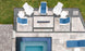 An aerial view of a modern patio shows six white chairs with blue cushions encircling a rectangular fire pit set on tile flooring with gravel accents, next to a small tiled pool. The scene includes the Mainstay Square Side Table by Ledge Lounger and nearby visible grass.