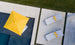 Aerial view of two white lounge chairs with EZ-Dri foam and Ledge Loungers Round Bolster Throw Pillows in yellow on a stone patio by a pool. A large yellow umbrella offers shade, vibrant outdoor fabrics are highlighted, and a green grass strip borders the patio.