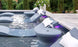 Submerged lounge chairs with white cushions and cup holders rest on a sun shelf under purple lights, perfect for in-pool use. The scene is enhanced by Ledge Loungers Signature Standard Side Table and a white flower arrangement among lush greenery.