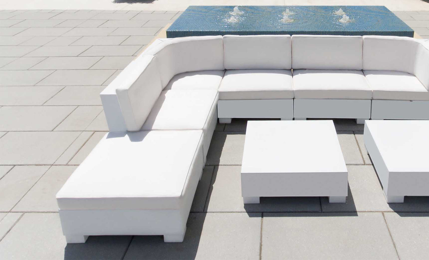 Arranged in an L-shape on a gray tiled patio, the Signature Sectional Corner by Ledge Lounger is paired with a matching square coffee table. Behind the sofa, a small rectangular fountain with gently flowing water enhances this outdoor oasis.