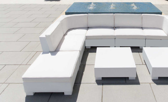 Arranged in an L-shape on a gray tiled patio, the Signature Sectional Corner by Ledge Lounger is paired with a matching square coffee table. Behind the sofa, a small rectangular fountain with gently flowing water enhances this outdoor oasis.