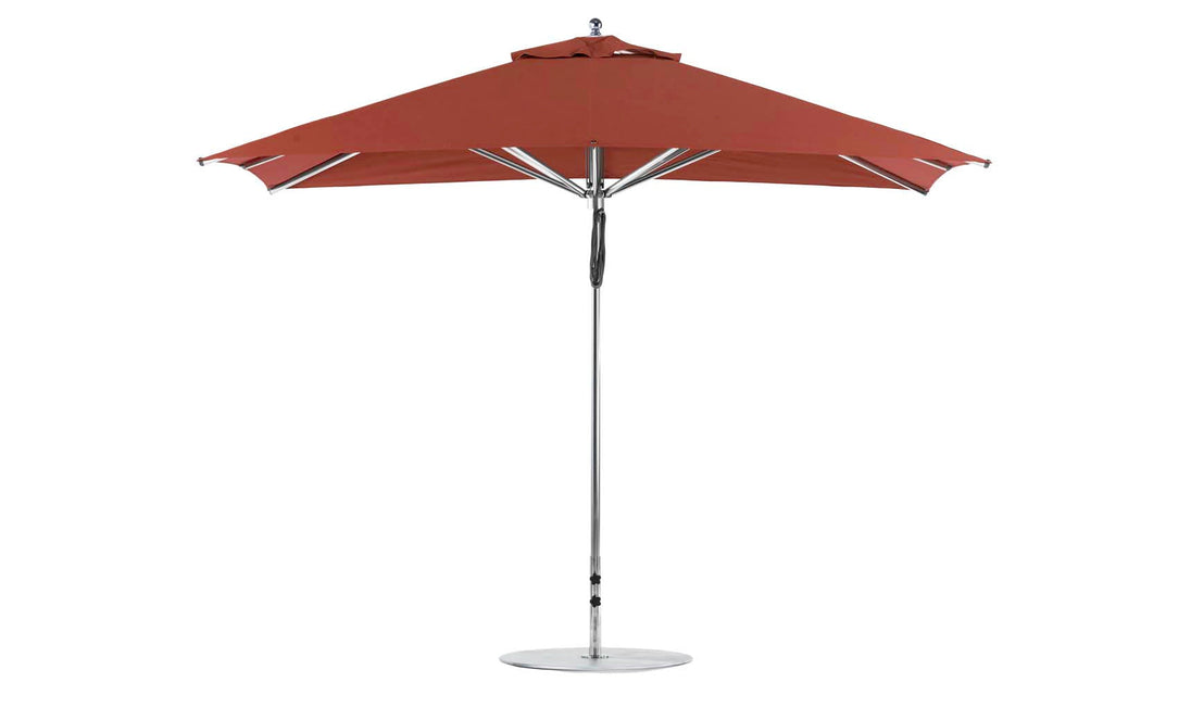 The 8.5 Ledge Loungers Premier Aluminum Umbrella, featuring a large red rectangle canopy made of marine-grade fabric and a vented top for wind resistance, stands upright with a sturdy metal pole and round base.