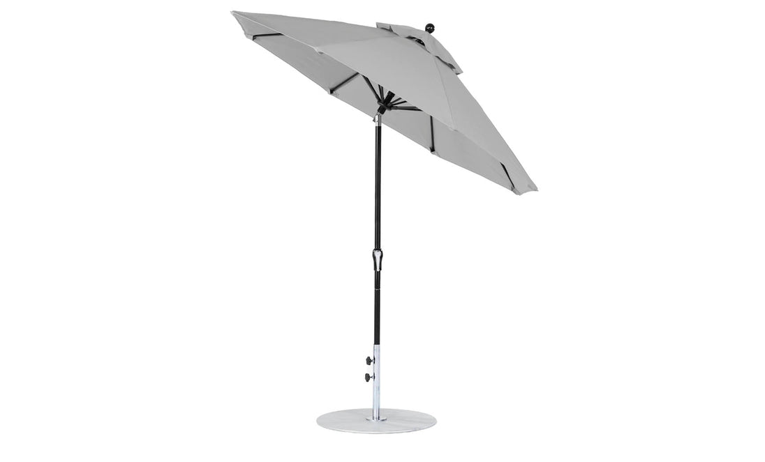 Against a plain white backdrop, the Essential Fiberglass Umbrella by Ledge Lounger, featuring a 7.5 octagon canopy in gray marine-grade fabric and a sleek black pole on a round metal base, highlights its design excellence with its partially open tilt position.
