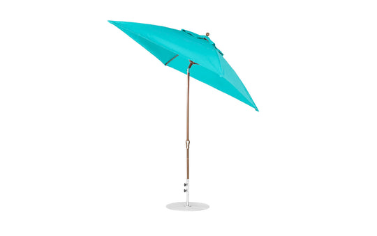 A turquoise Essential Fiberglass Umbrella, by Ledge Lounger, with wooden pole and metal base is shown open and tilted against a white background. This wind-resistant 7.5 octagon crank auto tilt umbrella features marine-grade fabrics for enhanced durability.