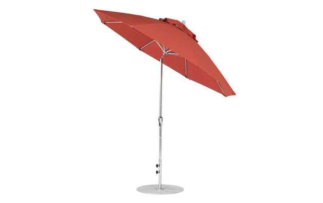 A red Ledge Lounger Essential Fiberglass Umbrella with a metal pole and round base is tilted slightly. Made from marine-grade fabrics, it showcases multiple supporting ribs when fully open. The 9 Octagon Crank Auto Tilt features an adjustable pole with a tilt mechanism for convenience.