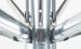 Close-up of the Premier Aluminum Umbrella - 10 Square Pulley by Ledge Lounger, showcasing its metallic structure with gleaming silver rods converging at a central point. The rods are secured with marine-grade fabrics and visible small screws. The background is a white blur.