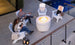 A man and woman relax on the patio in comfortable Adirondack chairs, enjoying wine by a lit fire pit table from the Halo Aglow Bundle by Ledge Lounger. Nearby is a pool, with decorative lights along the fence and lanterns enhancing the ambiance.